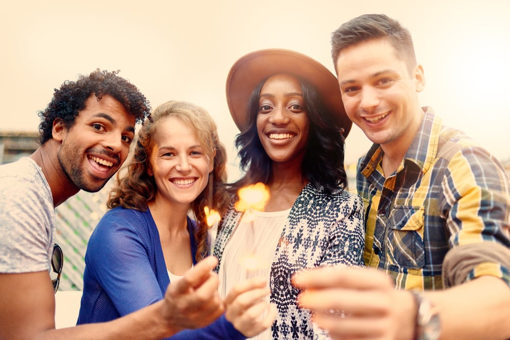 Multi-ethnic millenial group of friendsfolding sparklers on rooftop terrasse at sunset